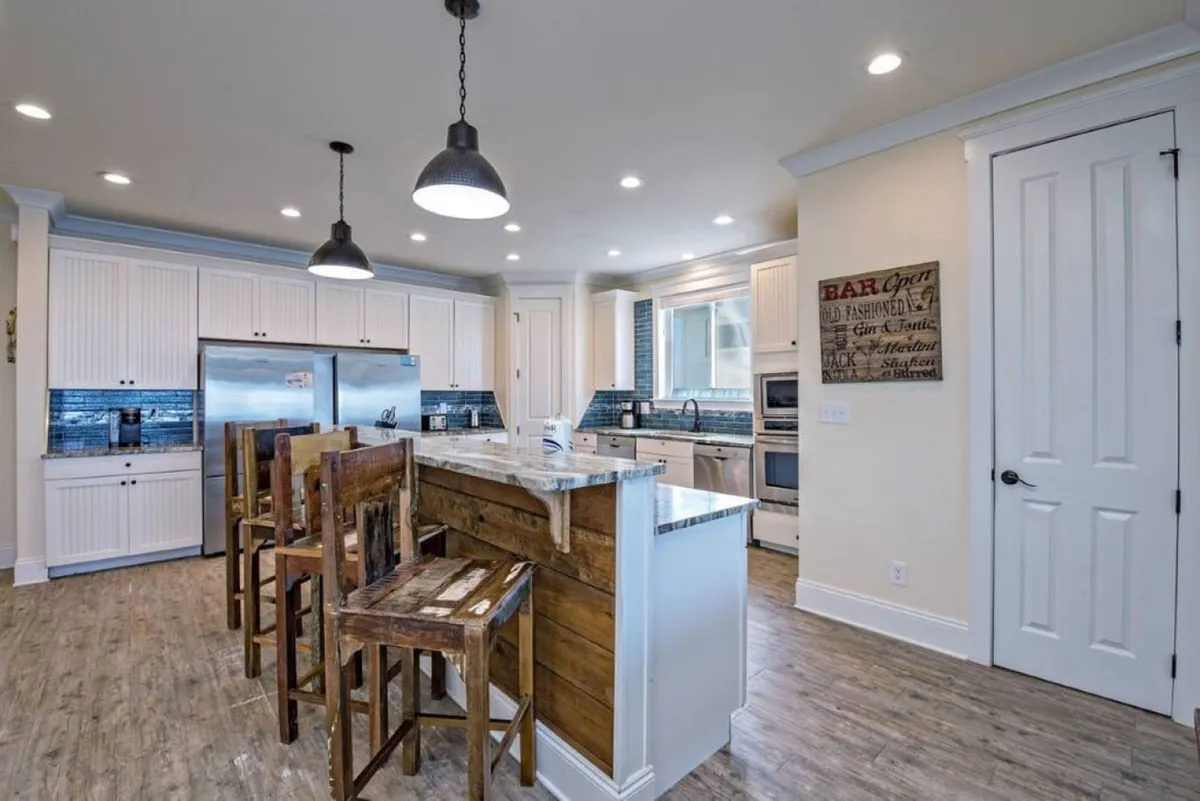 A modern kitchen with a central island and bar stools, stainless steel appliances, and expansive windows letting in abundant natural light. The setting is inviting for meal preparation, casual dining, and entertaining guests.