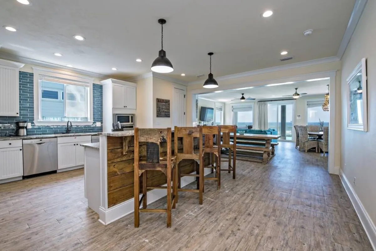 This image showcases a spacious, open kitchen with a large island and bar stools, a cozy dining area, and expansive windows that offer stunning views of the ocean. The layout clearly demonstrates the open-concept flow between the kitchen and dining area, filled with natural light and inviting for social gatherings.