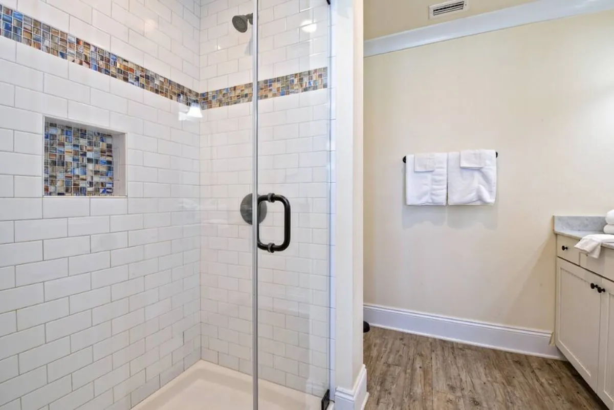 A modern bathroom featuring a glass shower enclosure, colorful mosaic accent strip, and high-end fixtures. The space feels refreshing and spa-like, ideal for both energizing mornings and calming evenings.