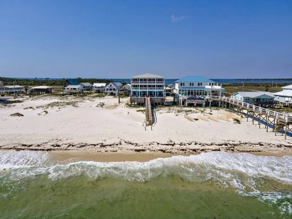 This image features a large beachfront house with multiple stories and balconies, a long wooden boardwalk leading directly from the house to the sugar-white sandy beach, and the calm Gulf of Mexico waters stretching out with gentle waves. The spacious outdoor areas and direct access to the sand are highlighted, with a tranquil, luxurious beachside atmosphere.